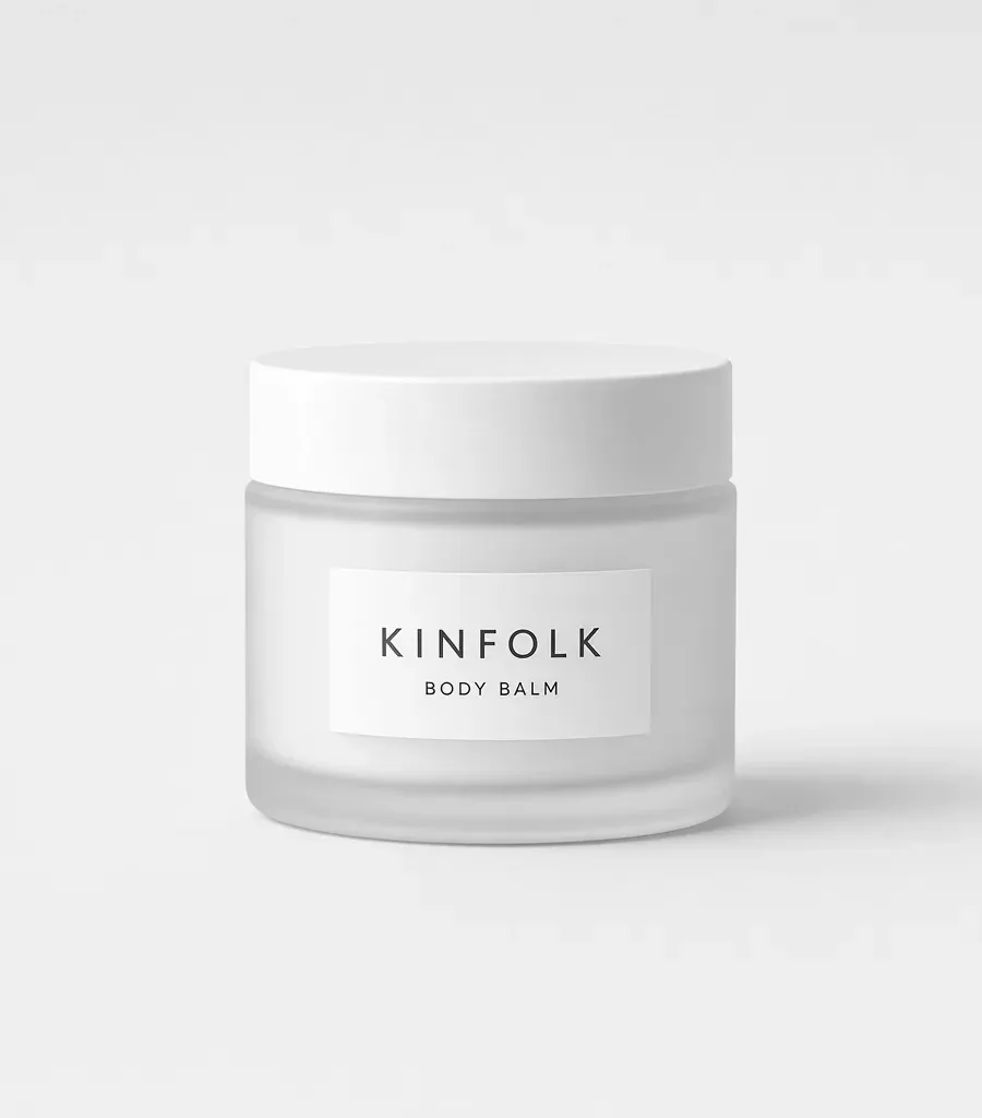 Frosted glass jar with a white lid and a label reading Kinfolk body balm