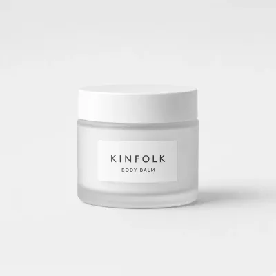 Frosted glass jar with a white lid and a label reading Kinfolk body balm