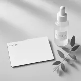 White Kinfolk gift card on linen beside a frosted face oil bottle and a sprig of eucalyptus