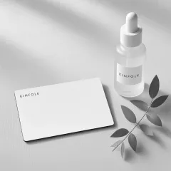 White Kinfolk gift card on linen beside a frosted face oil bottle and a sprig of eucalyptus