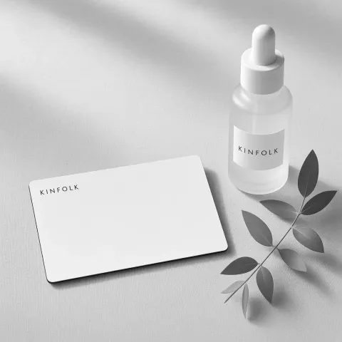 White Kinfolk gift card on linen beside a frosted face oil bottle and a sprig of eucalyptus