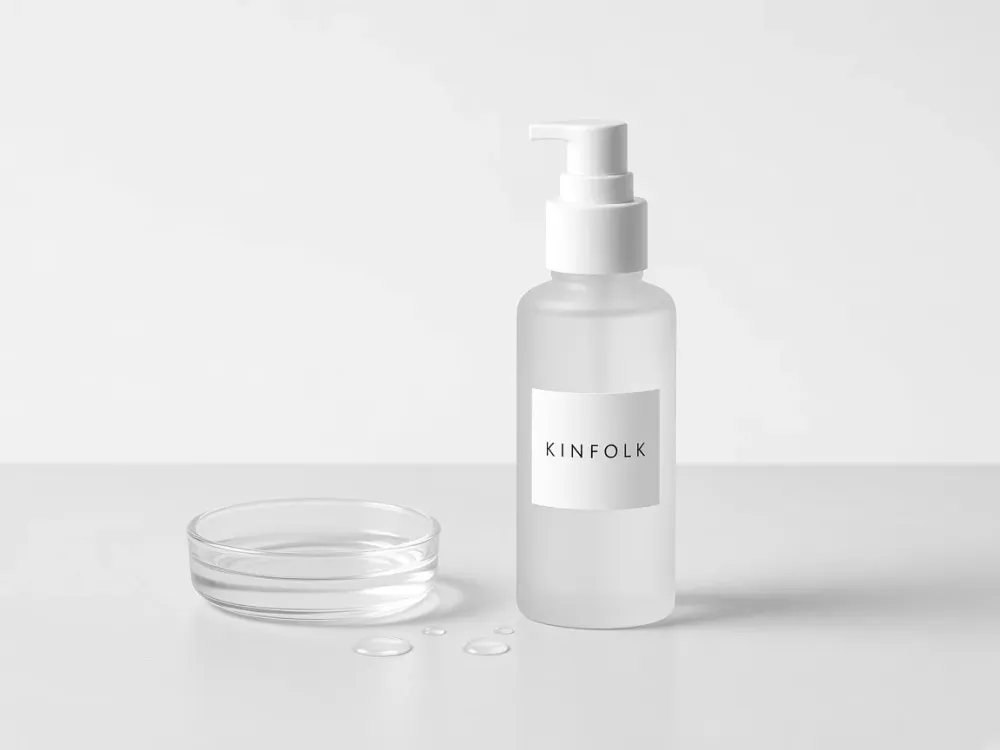 A frosted Kinfolk bottle beside a glass dish of clear tonic and a few droplets